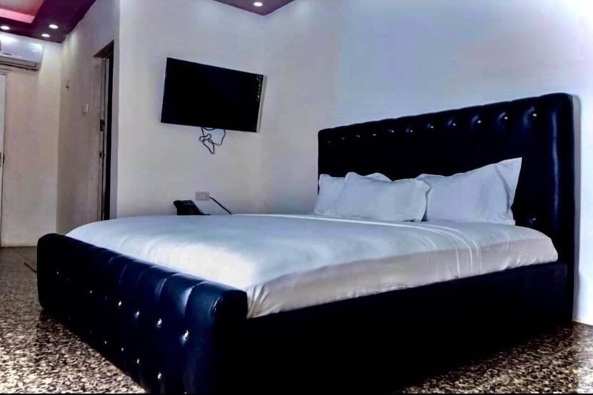A bedroom with a large bed, a flat-screen TV mounted on the wall, and a carpeted floor.