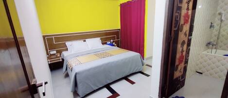 A hotel room with a bed, a shower, and a red curtain.