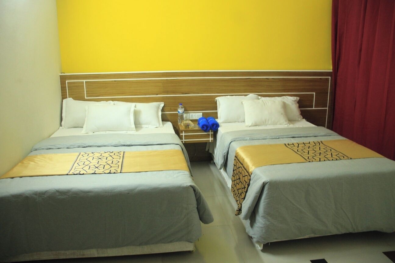A hotel room with two beds, each with a wooden headboard and white bedding. There is a nightstand with a water bottle and blue towels.