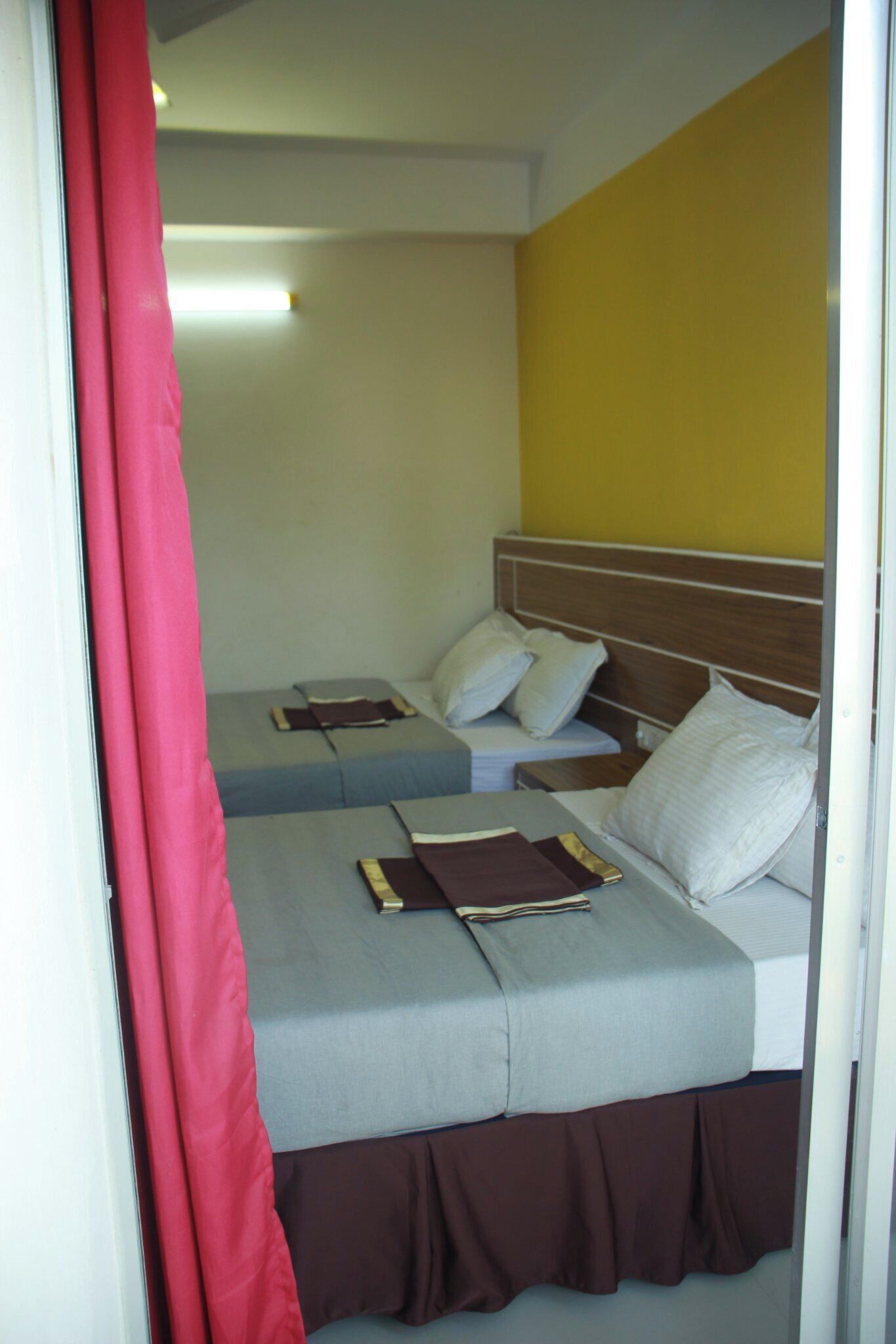 Habitación de hotel con dos camas, cabecero de madera y pared de acento amarilla.