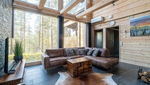 A modern log cabin interior with a large sectional sofa, a wooden chest, and a television on a wooden table. - Oivangin Lomakartano (Kuusamo)
