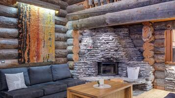 A log cabin interior with a stone fireplace, a gray sofa, and a wooden coffee table.