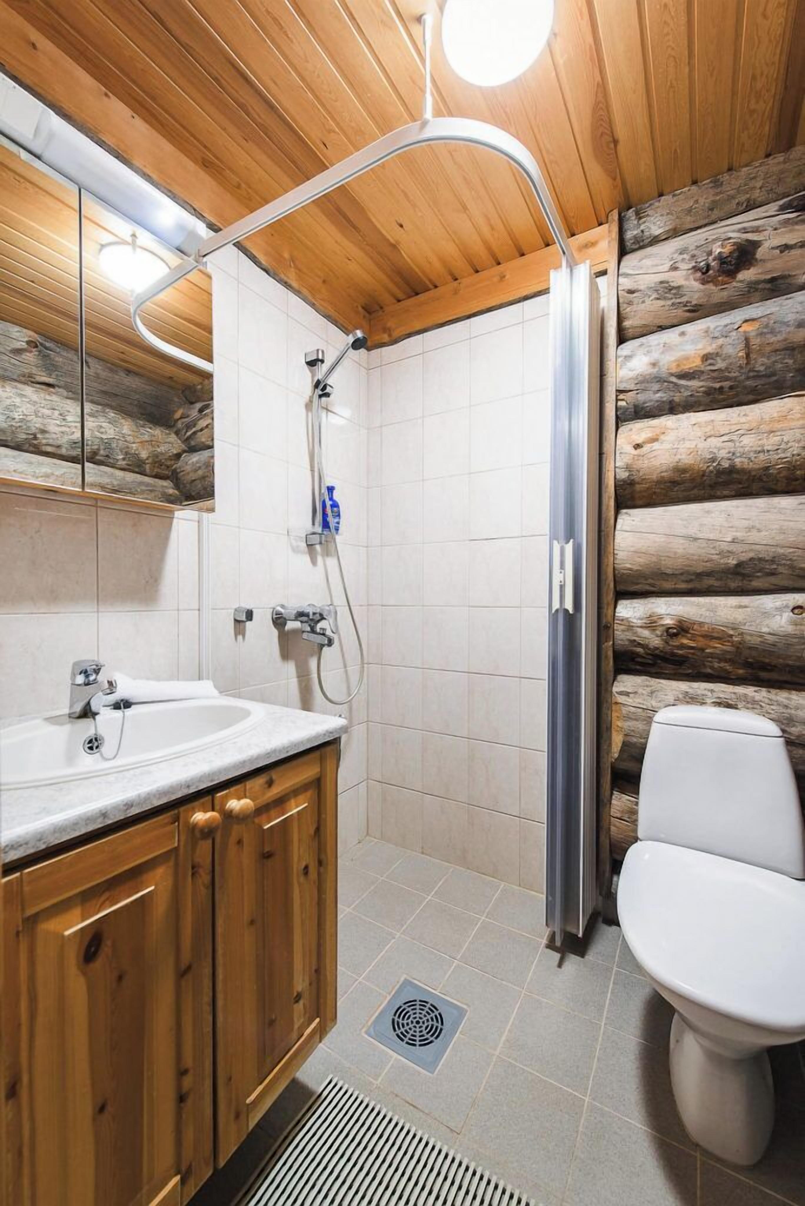 Ein Badezimmer mit Holzboden, einem Waschbecken mit Spiegel, einer Dusche und einer Toilette.