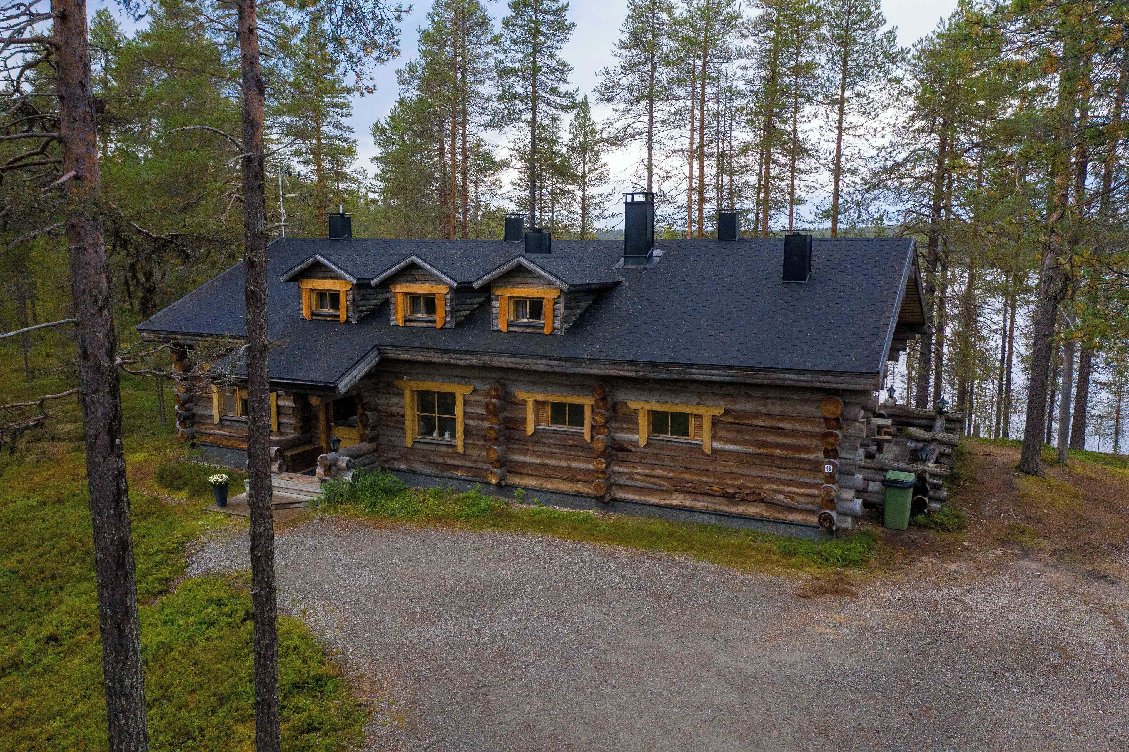 A log cabin with a gravel driveway, wooden windows, and a chimney.