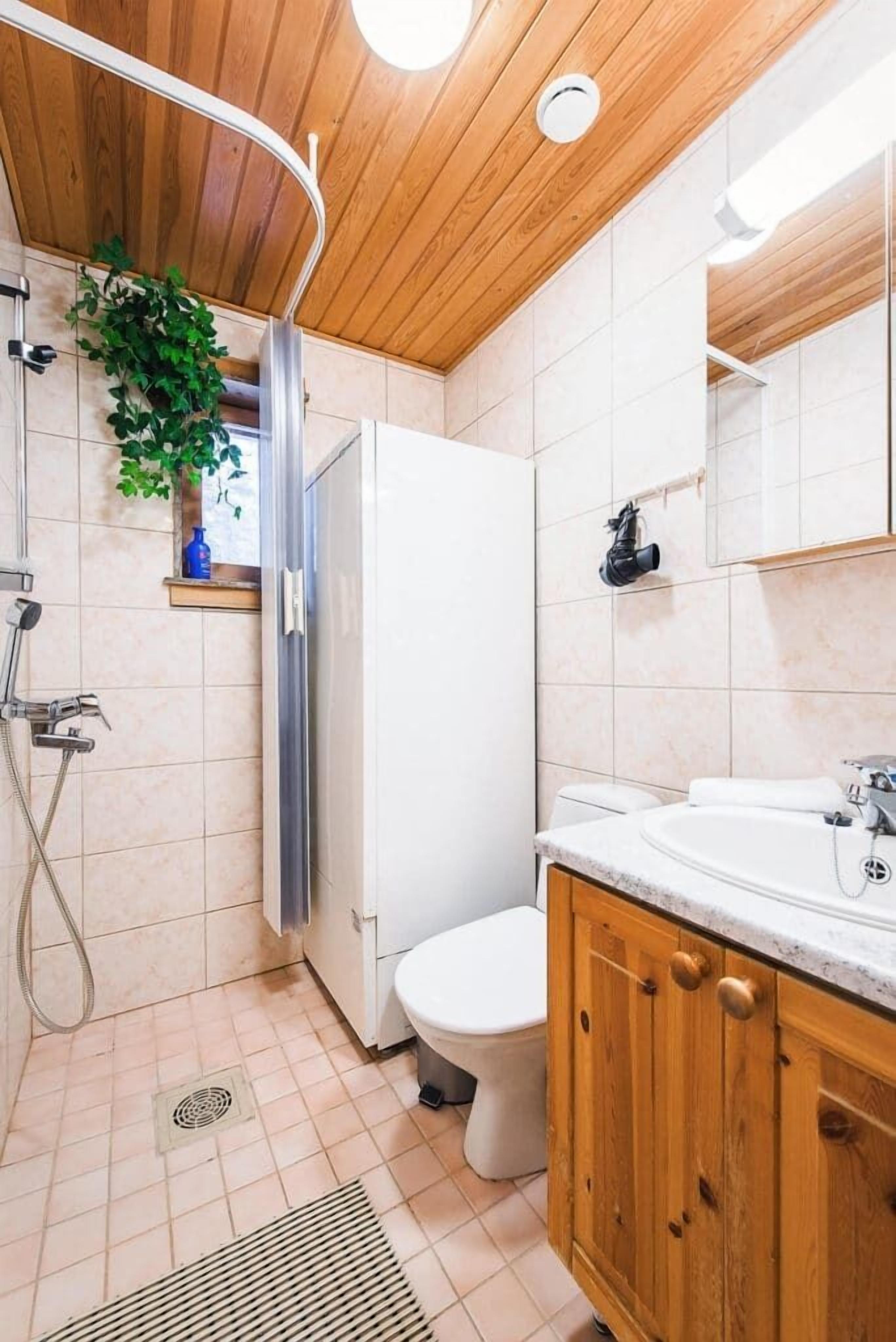 A bathroom with a wooden ceiling, a shower, a toilet, and a sink with wooden cabinets.