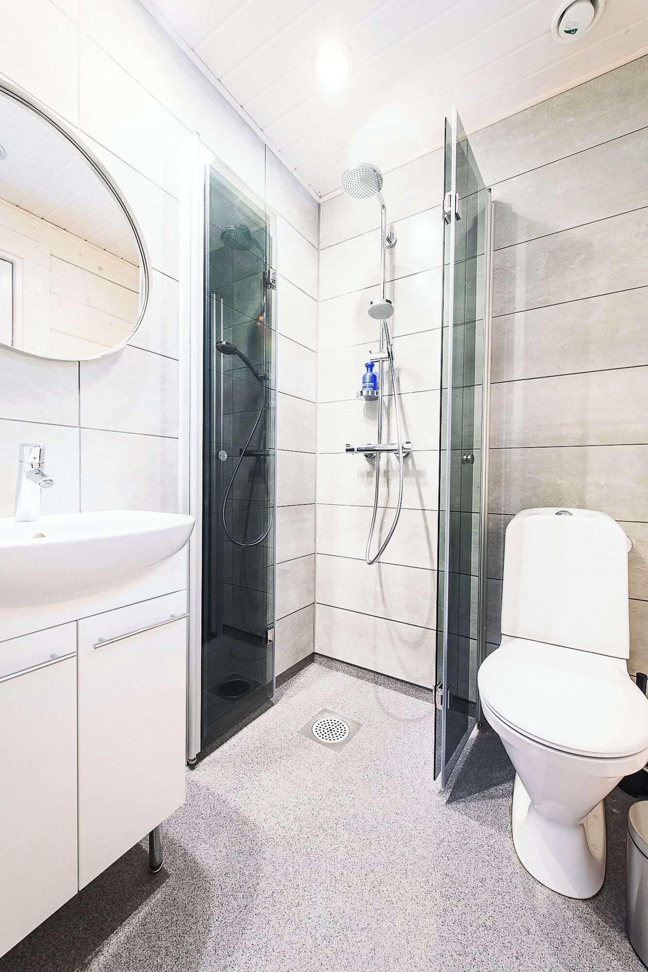 Un baño moderno con ducha de vidrio, un lavamanos blanco y un inodoro.