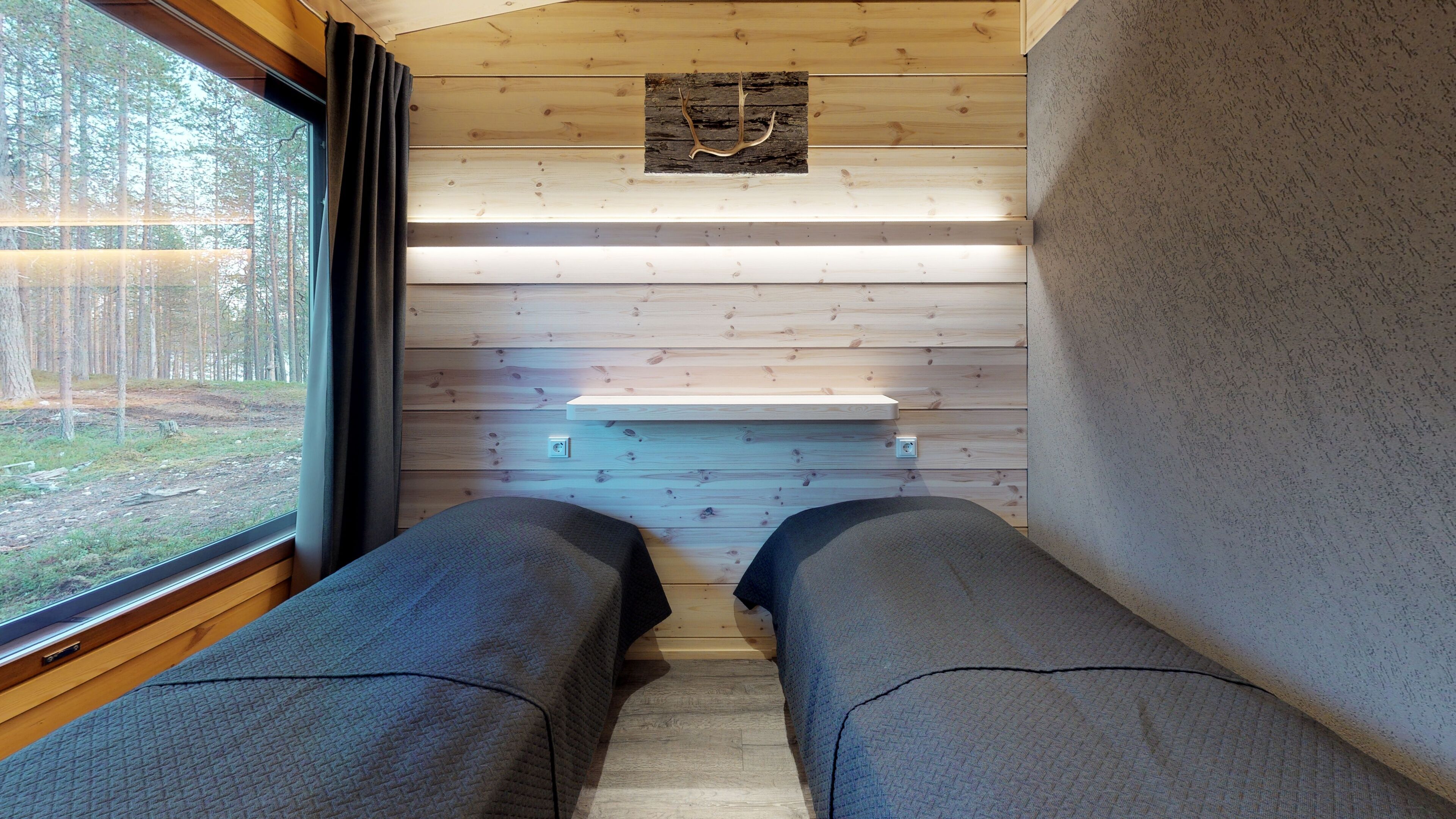 A cabin interior with two beds, a wooden ceiling, a shelf with a decorative item, and a window with curtains.