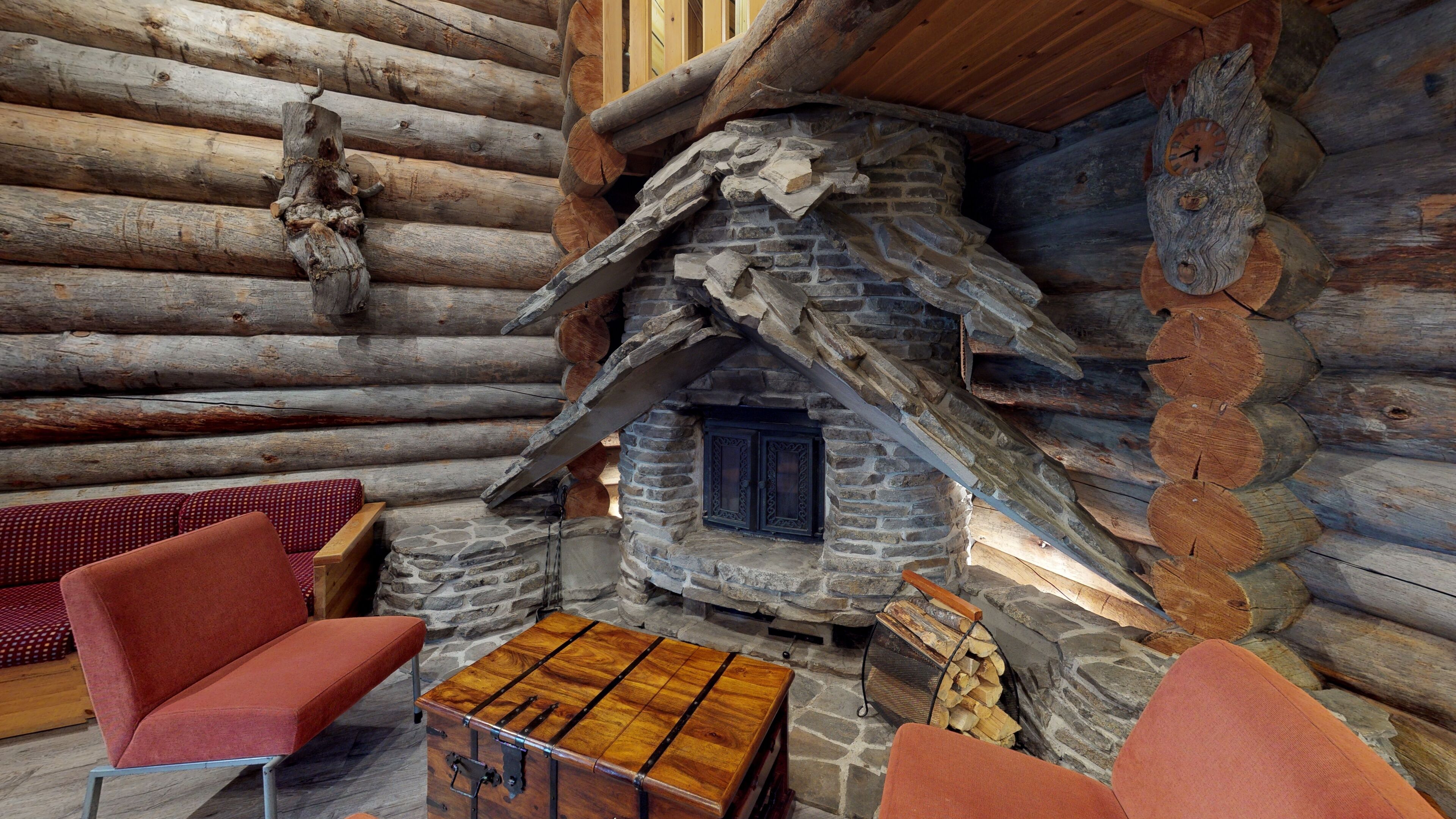A log cabin interior with a stone fireplace, wooden furniture, and a rustic aesthetic.