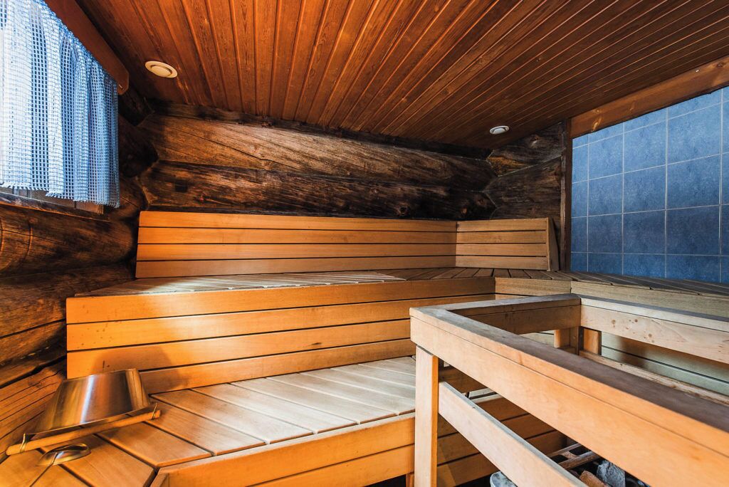 Een sauna met houten banken en een metalen emmer, met een rustieke stenen muur en houten plafond.