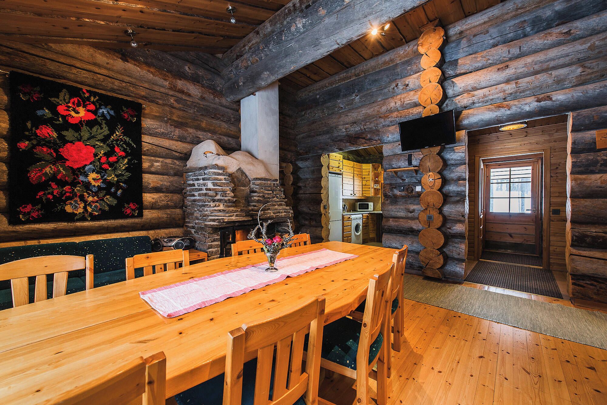 Interior de una cabaña de madera con comedor, chimenea de piedra y cocina.