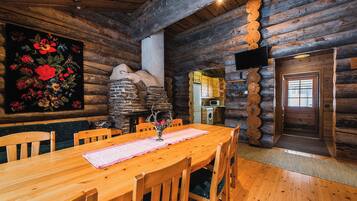 Interior de una cabaña de madera con comedor, chimenea de piedra y cocina.