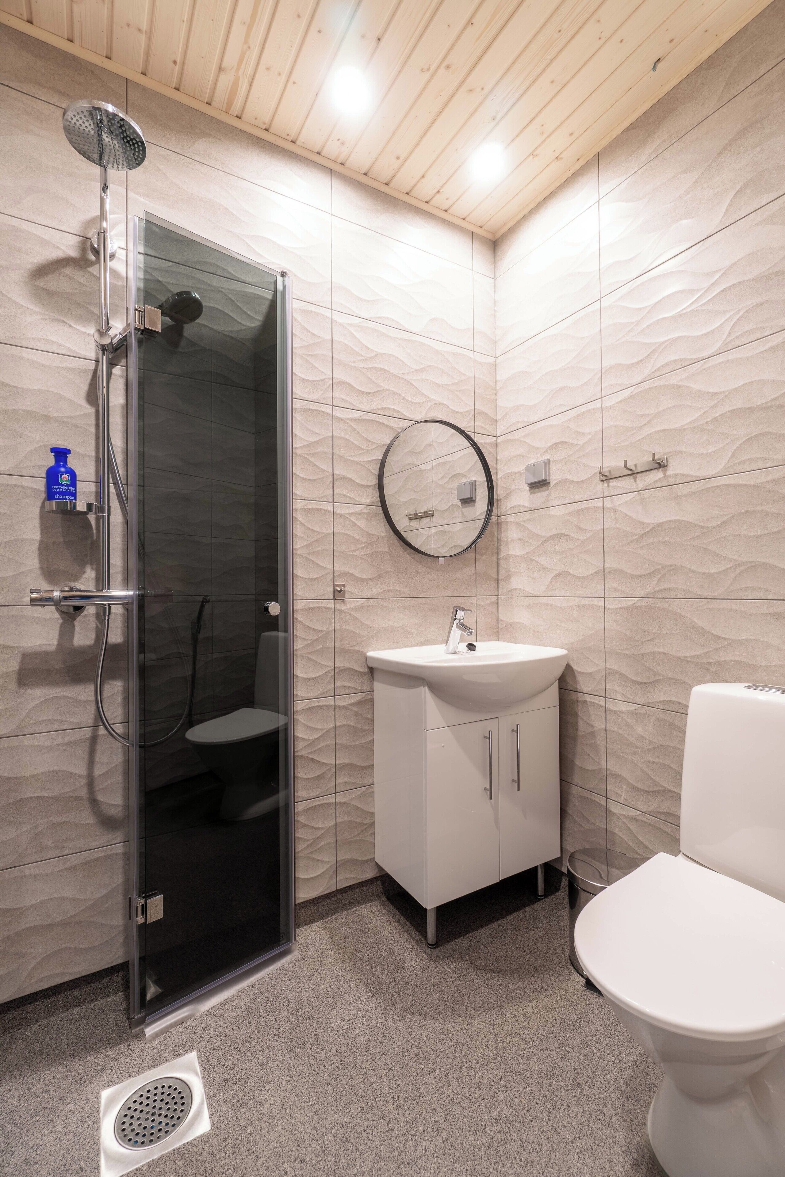 A modern bathroom with a glass-enclosed shower, a white sink, and a toilet.