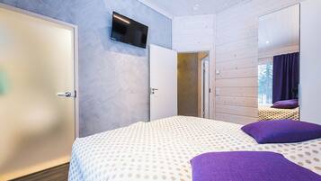 A bedroom with a bed, a TV mounted on the wall, and a door leading to another room.