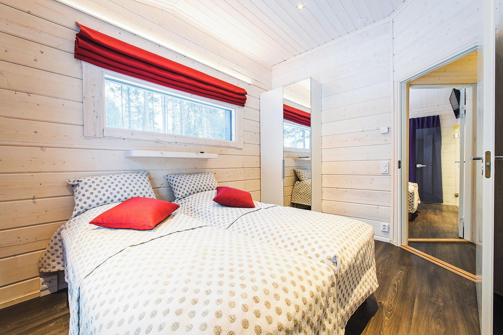 A bedroom with a bed, red curtains, a window, and a door.