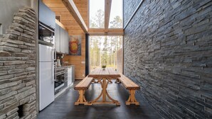 A modern kitchen with stone walls, a wooden table, and a view of the forest. - Oivangin Lomakartano (Kuusamo)