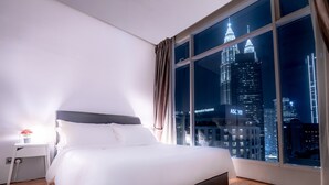 A hotel room with a large window offering a nighttime view of a city skyline, including a prominent illuminated tower. - Soho Suites KLCC (Kuala Lumpur)