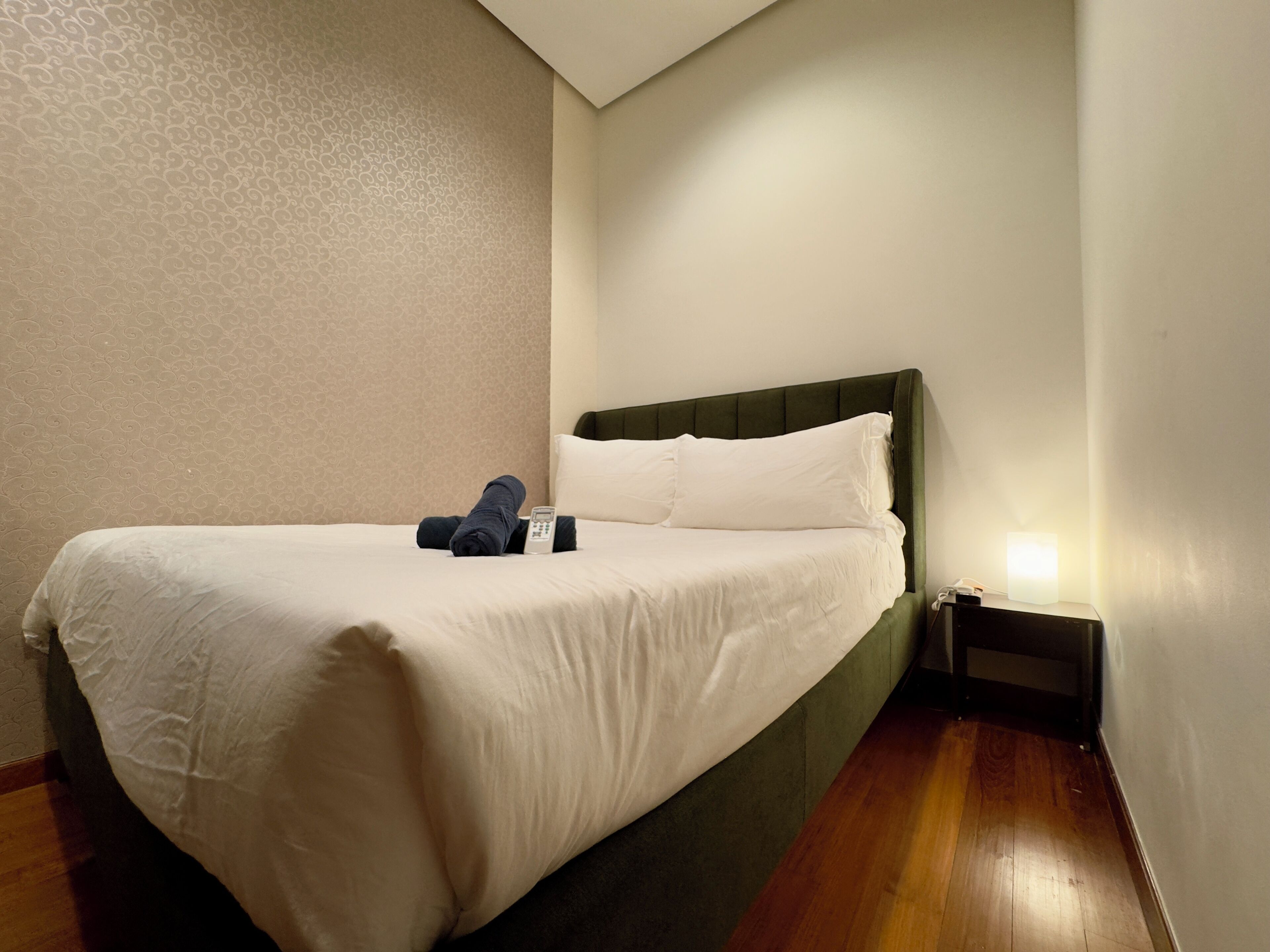 Una cama bien hecha con sábanas blancas, un cabecero verde y un control remoto sobre la cama.