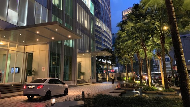 A modern hotel entrance with glass facade, palm trees, and a paved walkway. - Soho Suites KLCC (Kuala Lumpur)