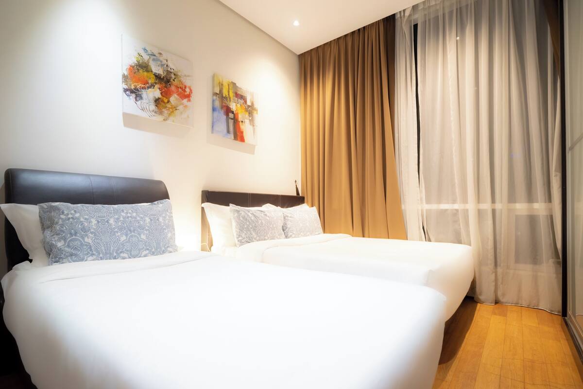 A hotel room with two beds, a large window with sheer curtains, and abstract art on the wall.
