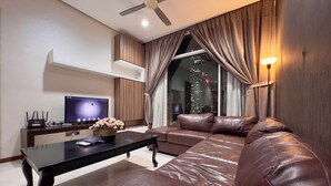 A modern living room with a leather sofa, a coffee table, a TV, and a ceiling fan. - Soho Suites KLCC (Kuala Lumpur)