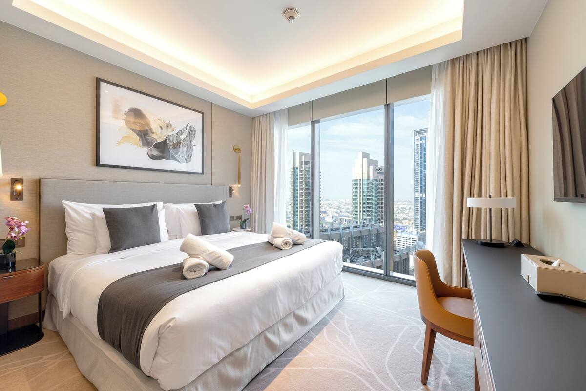 A modern hotel room with a large bed, a desk, and a view of the cityscape.