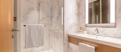 Une salle de bain moderne dotée d’une douche à parois de verre, d’un mur recouvert de carreaux de marbre, d’un grand miroir et d’un meuble-lavabo en bois.