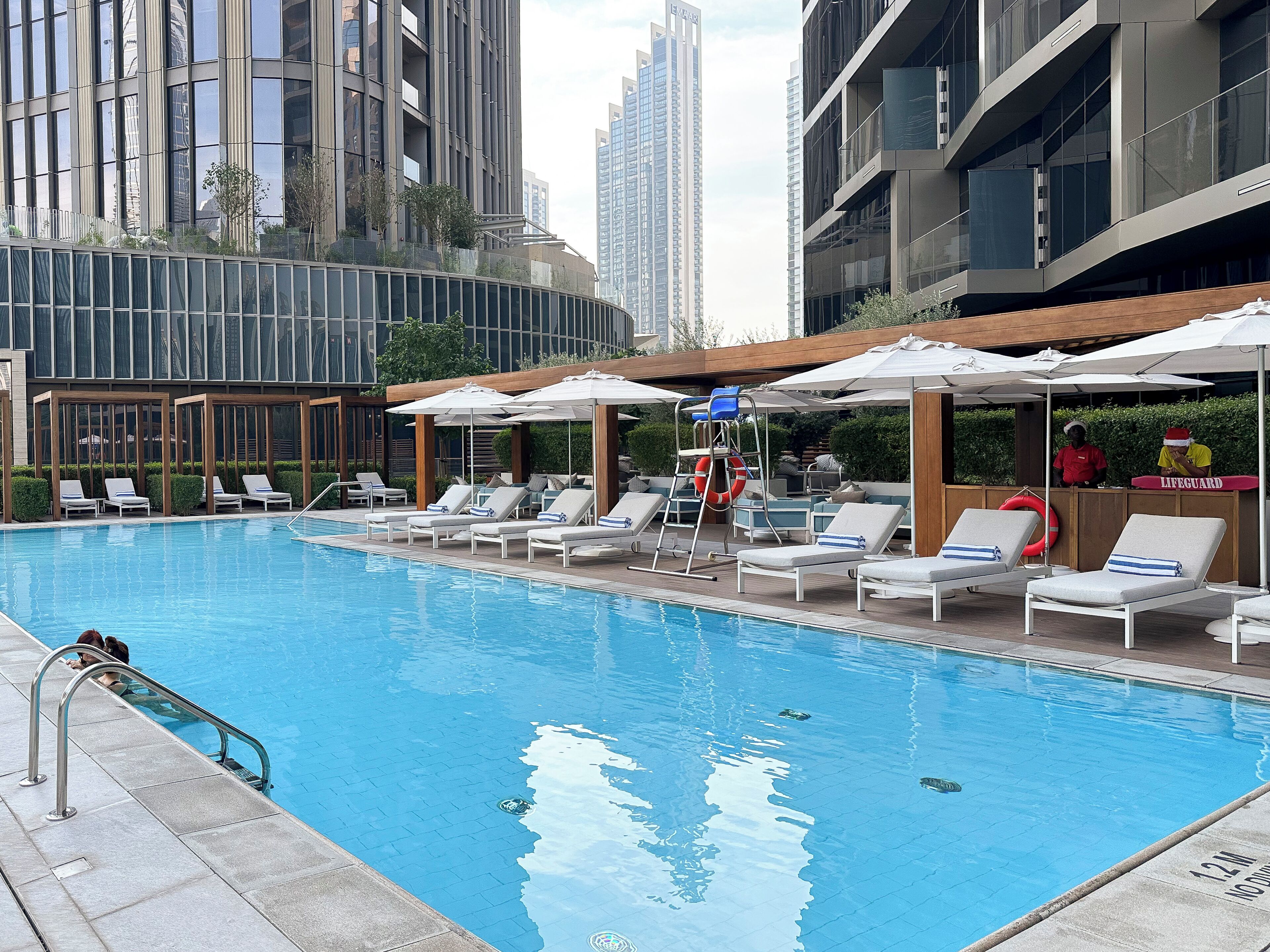 A swimming pool with lounge chairs and umbrellas, surrounded by modern buildings.