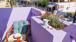 A balcony with a purple wall, a wicker chair, a table with fruits, a hat, and a mug. - THENA apartment in  Limenas Chersonisou (Limenas Chersonisou)