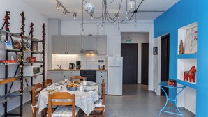 A modern kitchen with white cabinets, a dining table set with plates and a bowl of fruit, and a blue accent wall. - THENA apartment in  Limenas Chersonisou (Limenas Chersonisou)