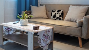 A living room with a sofa, a table with a floral tablecloth, a potted plant, and a remote control. - THENA apartment in  Limenas Chersonisou (Limenas Chersonisou)
