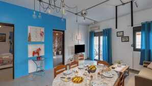 A dining area with a table set for four, a television, and a blue wall. - THENA apartment in  Limenas Chersonisou (Limenas Chersonisou)