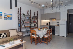 A modern kitchen with white cabinets, a dining table with chairs, and a sofa with a decorative plant.