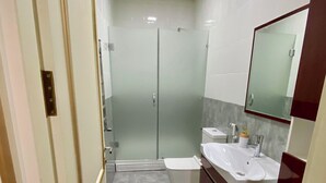 Un bagno moderno con box doccia in vetro, lavandino bianco e mobile contenitore con specchio.