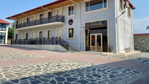 Un edificio a due piani con un balcone, una insegna che indica che si tratta di un albergo e un marciapiede con motivo in pietra di fronte.