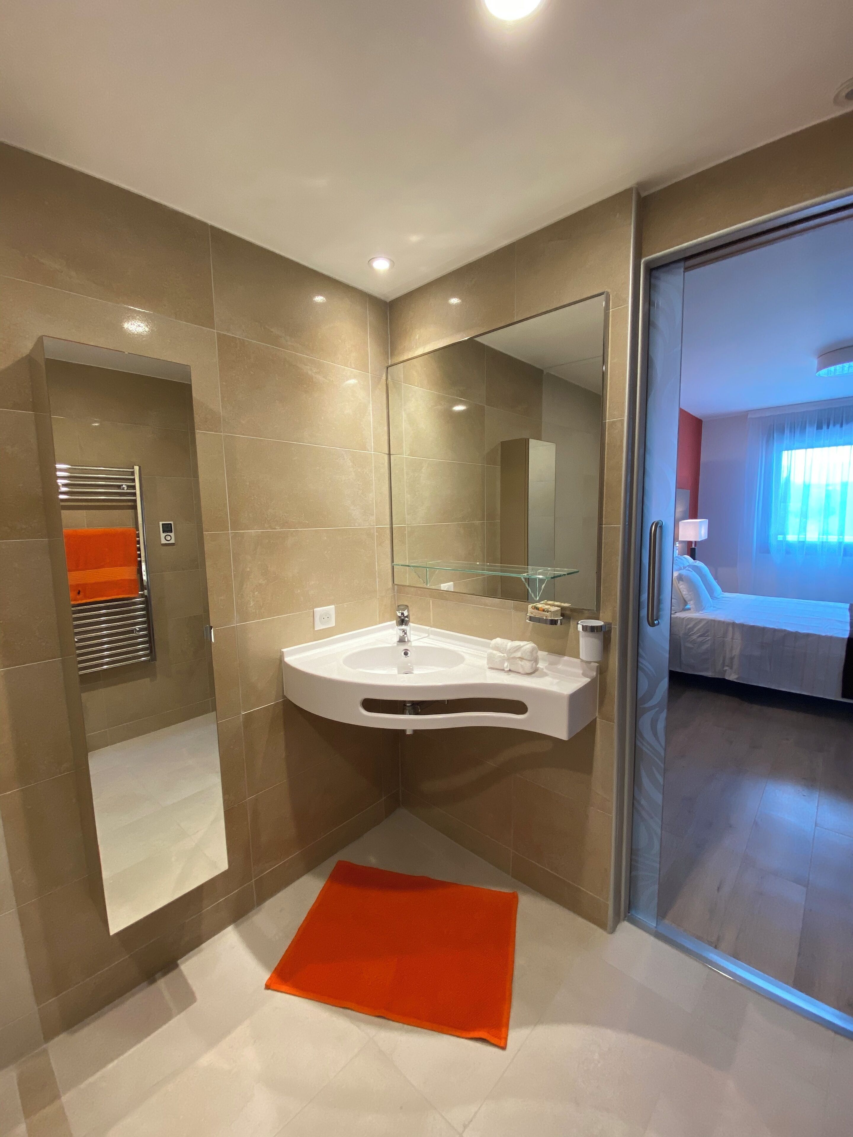 Une salle de bain moderne avec un grand miroir, un lavabo blanc et une cabine de douche en verre.