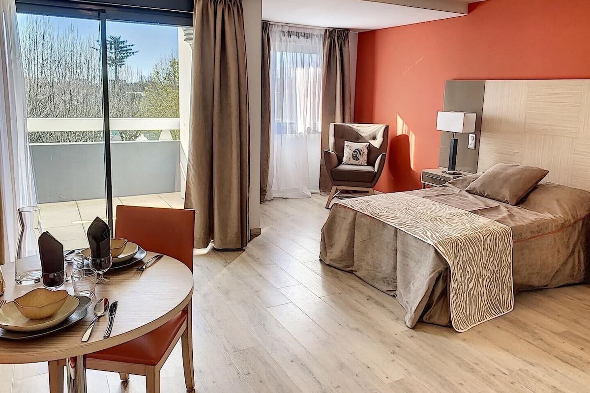 Une chambre d’hôtel avec un lit, une chaise, une table avec des couverts et une vue sur l’extérieur.