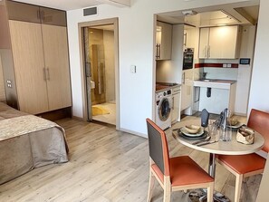 Une chambre d’hôtel compacte comprenant un lit, une petite kitchenette, un lave-linge et un coin repas avec une table et des chaises.