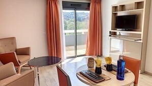 A hotel room with a sofa, a round table, a TV on a shelf, and a view through the glass door. - Appart One Le Cannet (Le Cannet)