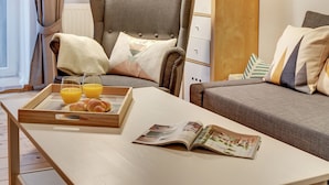 Una habitación acogedora con un sillón gris, un sofá, una mesa de madera con provisiones para el desayuno y una revista.
