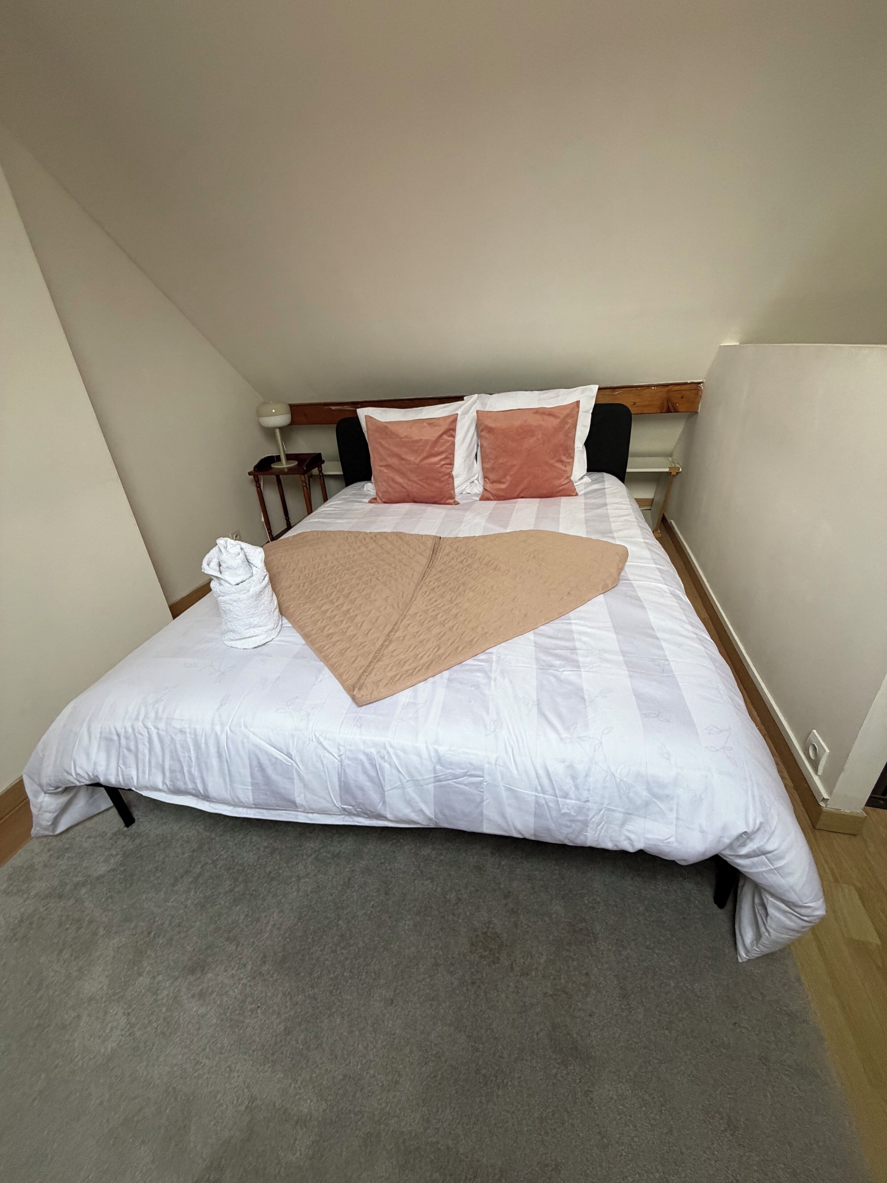Een netjes opgemaakt bed met een witte deken, twee kussens en een bruine plaid.