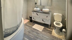 A modern bathroom with a curved bathtub, a vanity with two sinks, a toilet, and a large mirror.