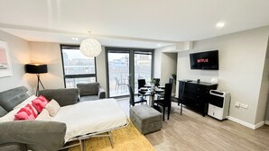 A modern apartment with a bed, sofa, dining area, and a TV displaying Netflix. - 3-Bed Hoxton Flat w/ Private Balcony & Lift access near Shoreditch , Old Street (London)