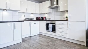 A modern kitchen with white cabinetry, a dishwasher, a built-in oven, and a stainless steel range hood. - 3-Bed Hoxton Flat w/ Private Balcony & Lift access near Shoreditch , Old Street (London)