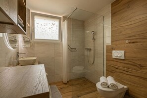 A modern bathroom with a glass-enclosed shower, a wooden vanity, and a toilet with towels. - Apartments Natura Apartments (Črnomelj)