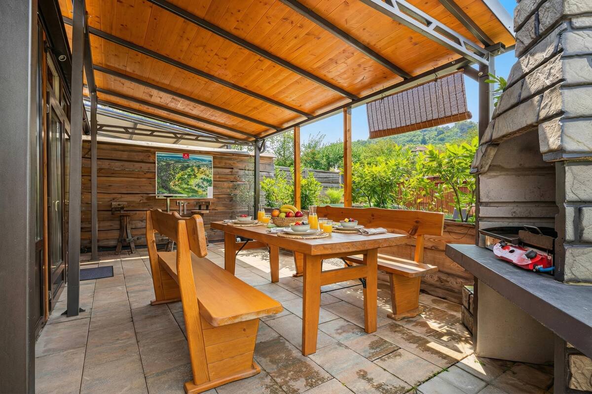 Une terrasse extérieure avec des meubles en bois, une cheminée en pierre et une vue sur la verdure.