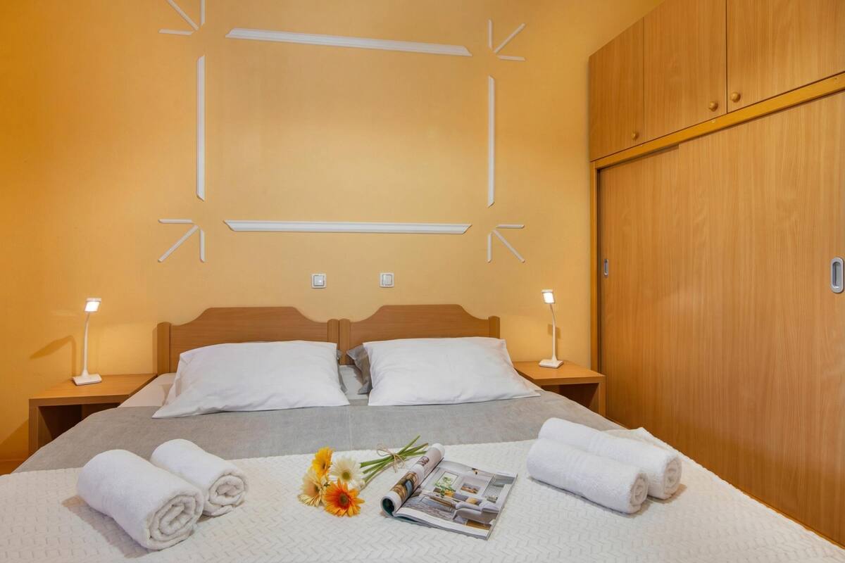 Une chambre d’hôtel avec un lit, deux lampes de chevet, une armoire en bois et un mur orné de luminaires aux formes géométriques.