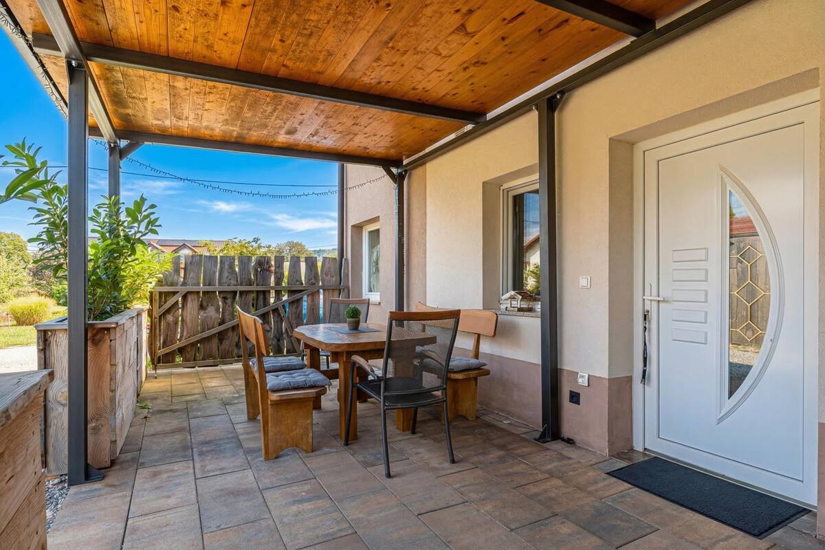 Une terrasse couverte avec une table et des chaises, une clôture en bois et une porte avec une fenêtre.