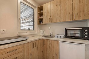 A kitchen with wooden cabinets, a built-in oven, a microwave, a sink, and a window with blinds.