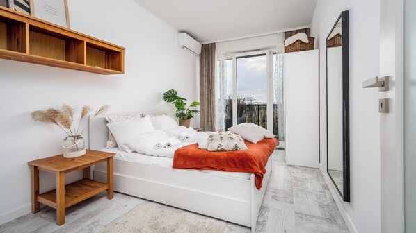 A bedroom with a bed, a bedside table, a potted plant, and a view of the outdoors.