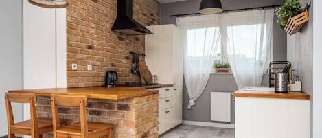 A kitchen with a brick wall, wooden bar counter, and white cabinets.